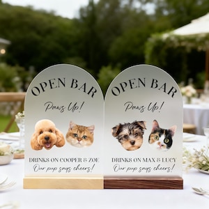 May include: Two arched signs with the text "OPEN BAR Paws Up!" feature dog and cat portraits. The signs read "DRINKS ON COOPER & ZOE Our pup says cheers!" and "DRINKS ON MAX & LUCY Our pup says cheers!" The signs are on wooden bases.