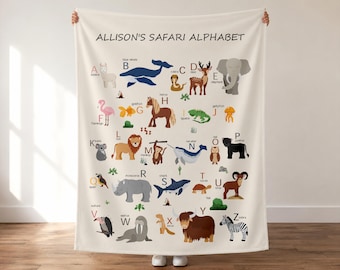 Könnte beinhalten: Eine cremefarbene Fleecedecke mit dem Text ALLISON'S SAFARI ALPHABET am oberen Rand. Die Decke zeigt ein bunt illustriertes Alphabet von A bis Z, wobei jeder Buchstabe mit einem passenden Tier kombiniert ist, wie A für Alpaka, B für Blauwal und Z für Zebra.