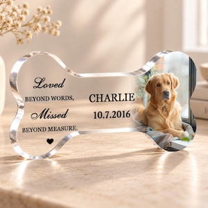 May include: A clear, bone-shaped acrylic memorial plaque featuring a photograph of a golden retriever. The text reads: Loved BEYOND WORDS, Missed BEYOND MEASURE. CHARLIE 10.7.2016, with a small black heart icon below the text.