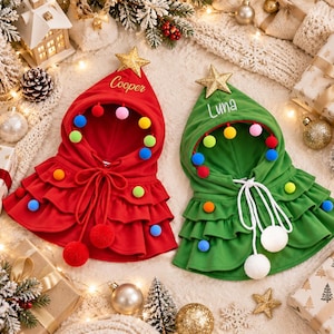 May include: Two hooded capes in red and green, each topped with a gold star. The red cape features the name Cooper, and the green cape features the name Luna. Both capes are decorated with colorful pom-poms, ruffled tiers, and white drawstrings.