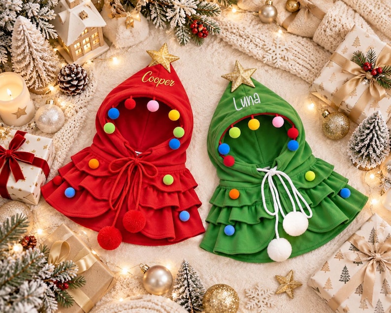 May include: Two hooded capes in red and green, each topped with a gold star. The red cape features the name Cooper, and the green cape features the name Luna. Both capes are decorated with colorful pom-poms, ruffled tiers, and white drawstrings.