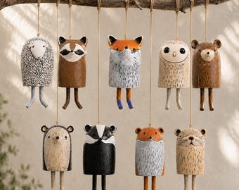 May include: A collection of nine hanging animal ornaments suspended from a wooden branch by twine. Each ornament features a cylindrical body with dangling legs, depicting a sheep, raccoon, fox, owl, bear, hedgehog, badger, and two other foxes.