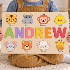 May include: A rectangular wooden name puzzle featuring the name ANDREW in large, colorful letters. Above and below the name are eight wooden animal face cutouts labeled Tiger, Hippo, Monkey, Duck, Mouse, Bear, Sheep, and Giraffe.