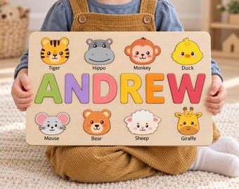 May include: A rectangular wooden name puzzle featuring the name ANDREW in large, colorful letters. Above and below the name are eight wooden animal face cutouts labeled Tiger, Hippo, Monkey, Duck, Mouse, Bear, Sheep, and Giraffe.