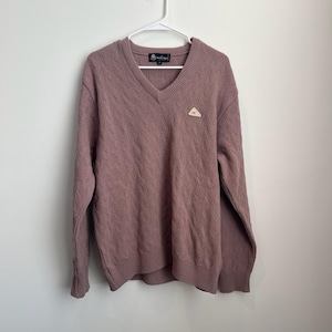 May include: Mauve V-neck sweater with a textured cable knit pattern. The sweater has long sleeves and a small emblem on the chest. It is hanging on a white hanger against a plain white background.
