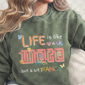 May include: A white ceramic mug with a black handle and the text "But First, Coffee" in a bold, black font. The mug is set against a blurred background, suggesting a cozy setting.