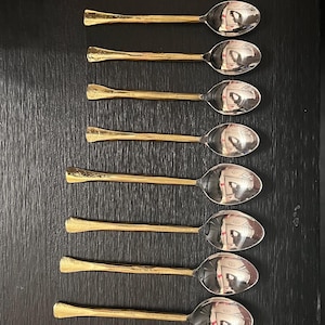 May include: A collection of elegant silverware, including forks, spoons, and knives. The utensils feature gold-colored handles and silver-colored blades and tines, arranged on a dark surface. A complete set for dining.