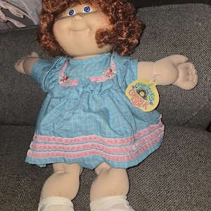 May include: A handmade wooden sign with the text "Welcome" in a whimsical font. The sign is painted white with a distressed finish, and features a decorative floral design in shades of pink and green. It measures approximately 12 inches wide.