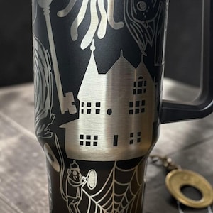 May include: A white ceramic mug with a black handle and the text "But First, Coffee" in a bold, black font. The mug is set against a blurred background, suggesting a cozy setting.