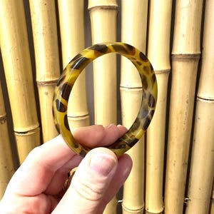 May include: A brown and yellow tortoiseshell bangle bracelet. The bracelet is made of plastic and has a smooth, glossy finish.