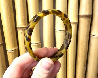 以下が含まれることがあります： 茶色と黄色のべっ甲柄のバングルブレスレット。プラスチック製で、滑らかで光沢のある仕上げです。
