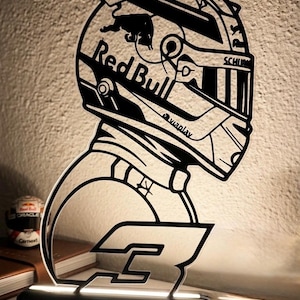 Könnte beinhalten: Eine schwarz-weiße LED-Lampe aus Acryl in Form eines Rennhelms mit dem Red Bull-Logo, dem Text Viaplay und der Nummer 3. Das Design zeigt ein detailliertes Helmprofil mit Visier und einem Sockel, der die klare Acrylstruktur beleuchtet.