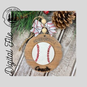 Peut inclure: Une décoration ronde en bois avec un motif de baseball et le texte "And God created a Coach". La décoration est ornée d'un nœud en ruban rouge et blanc.