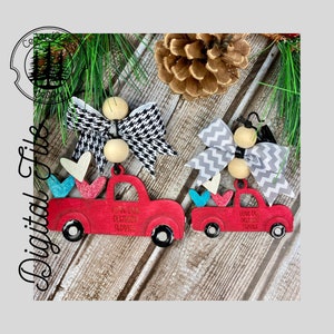 Può includere: Due ornamenti di camion in legno rosso con ruote bianche e dettagli neri. Ogni camion ha un fiocco in cima e trasporta cuori nella cassa. Il testo "Love ya Delivery Service" è sul lato di ogni camion.