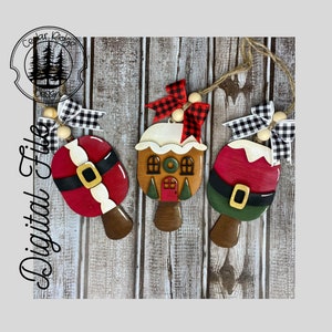 May include: Three wooden Christmas ornaments, each with a different design. One is a gingerbread house with a green door and white frosting. Another is a Santa Claus with a red hat and white beard. The third is a snowman with a black hat and a carrot nose. Each ornament has a black and white checkered ribbon and a wooden bead.