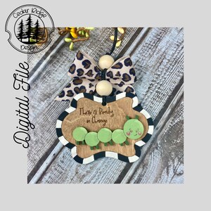 Può includere: Sagoma di legno di un bruco con il testo "There is Beauty in Change" su uno sfondo marrone con strisce bianche e nere. La sagoma è attaccata a un nastro leopardato marrone e nero con perline di legno.