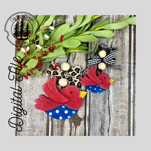 May include: Two red and blue bird ornaments with white polka dots. The birds are hanging from wooden beads and ribbon. The larger bird has a black and white checked bow and the smaller bird has a leopard print bow.