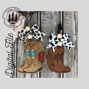 May include: Two pairs of brown cowboy boot ornaments with different designs. One pair has a floral design with red, blue, and green accents. The other pair has a floral design with brown and white accents. Both pairs have a wooden bead and a bow attached.