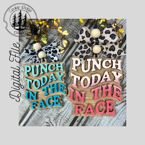 Op de afbeelding: Twee houten ornamenten met de tekst "Punch Today In The Face" in verschillende kleuren. Het bovenste ornament heeft blauwe tekst en het onderste ornament heeft roze tekst.