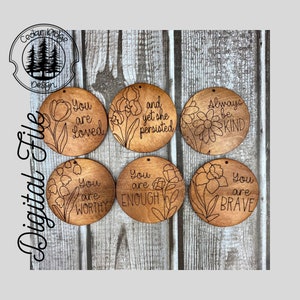 May include: Six round wooden ornaments with laser-etched floral designs and inspirational messages. The messages include "You are loved", "and yet she persisted", "Always be kind", "You are worthy", "You are enough", and "You are brave".