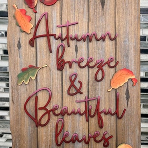 May include: Wooden sign with a rustic brown finish and red lettering that reads "Autumn breeze & Beautiful leaves". The sign is decorated with several colorful fall leaves.