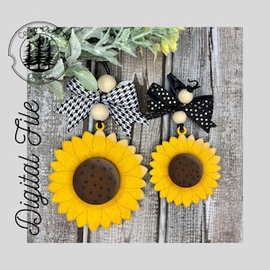 Può includere: Due ornamenti di girasole in legno con fiocchi a scacchi bianco e nero e a pois. I girasoli sono gialli con centri marroni e punti neri. I fiocchi sono attaccati a perline di legno.