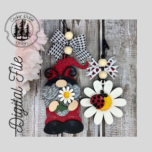 May include: A set of three wooden ornaments featuring a ladybug gnome holding a daisy, a ladybug on a daisy, and a black and white bow with wooden beads. The ornaments are painted in red, black, white, and yellow.