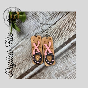 Puede incluir: Un par de pendientes de madera con un diseño de cinta rosa y corazón. Los pendientes son negros y rosas con lunares blancos.