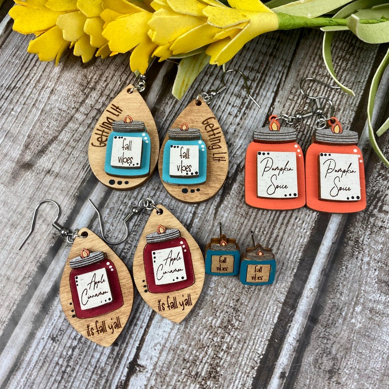 Puede incluir: Un conjunto de seis pendientes de madera con dise&ntilde;os de oto&ntilde;o. Los pendientes tienen forma de tarros con tapas y presentan varios dise&ntilde;os de oto&ntilde;o, incluyendo "Pumpkin Spice", "Apple Cinnamon" y "Fall Vibes".