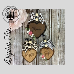 May include: Three wooden heart-shaped ornaments with different designs. The top ornament has a brown heart with the word "Mamaw" written on it. The middle ornament has a brown heart with the word "Daughter" written on it. The bottom ornament has a brown heart with the word "Sister" written on it.