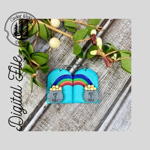 May include: A pair of wooden earrings with a rainbow and a pot of gold design. The earrings are blue with a silver pot of gold and gold coins. The text "Pot o Gold" is written on the pot.