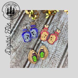 May include: Three pairs of wooden earrings shaped like potion bottles with glitter accents. The bottles are in blue, pink, and green. The earrings are on a wooden surface.