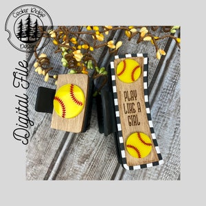 以下が含まれることがあります： 黒と白の市松模様の縁取りが施された木製のヘアクリップが2つ。1つのクリップには、赤いステッチの入った黄色のソフトボールと「PLAY LIKE A GIRL」の文字が書かれている。もう1つのクリップには、赤いステッチの入った黄色のソフトボールが描かれている。