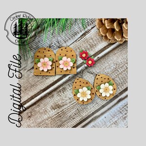 May include: A pair of wooden earrings with a pink and white flower design. The earrings are shaped like a teardrop and have a brown background with white polka dots.