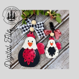 May include: Two wooden chicken ornaments with red, black, and white paint. The larger chicken has a black and white checkered bow and the smaller chicken has a red and white checkered bow. Both chickens have wooden beads on their strings.