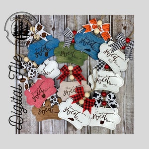 May include: A collection of 10 wooden ornaments featuring the text "Home Sweet Home" in various colours and styles. The ornaments are decorated with bows, beads, and other embellishments.