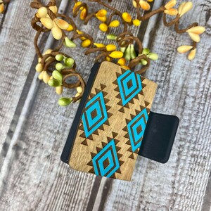 May include: A wooden phone grip with a blue and brown geometric pattern. The grip has a black silicone back.