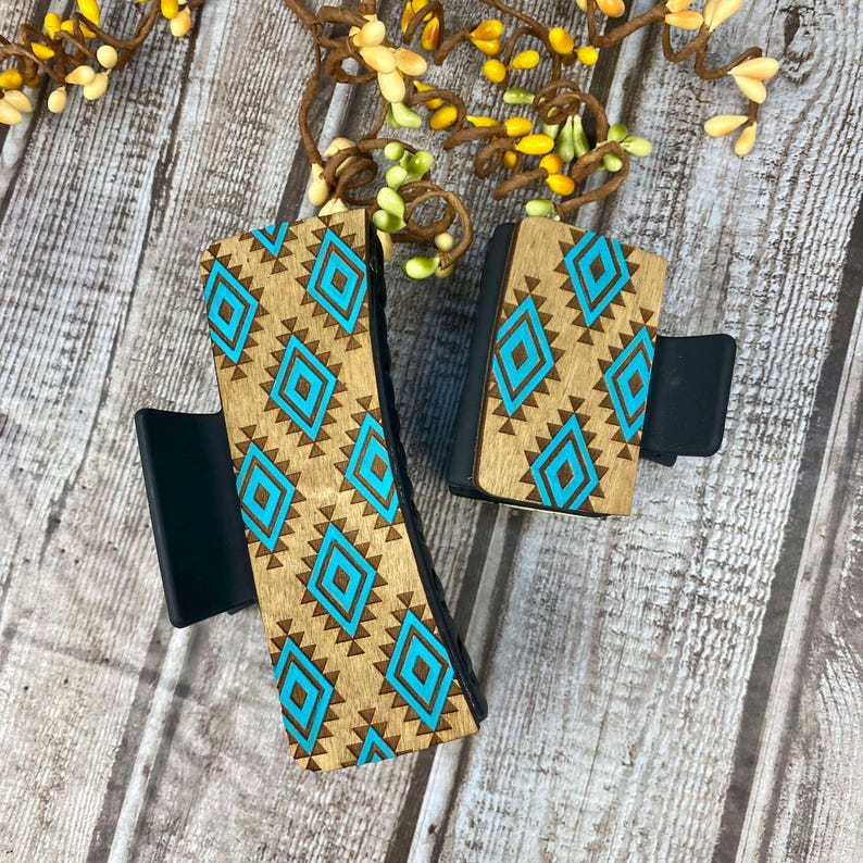 May include: Two wooden hair clips with a turquoise and brown geometric pattern. The clips are made of wood and have a black plastic base.