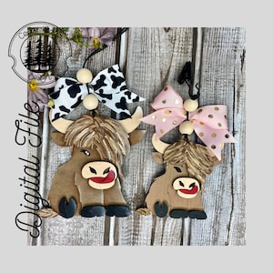 May include: Two wooden Highland Cow ornaments with black and white, and pink and gold bows. The ornaments are hanging from a string with wooden beads.