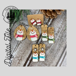 Puede incluir: Un conjunto de seis pendientes de madera con forma de muñeco de nieve. Dos pendientes presentan un muñeco de nieve con una bufanda rosa y el texto "Snow Happy" y "Snowman". Dos pendientes presentan un muñeco de nieve con una bufanda verde y el texto "Let It Snow". Dos pendientes presentan un muñeco de nieve con una bufanda azul y un copo de nieve.