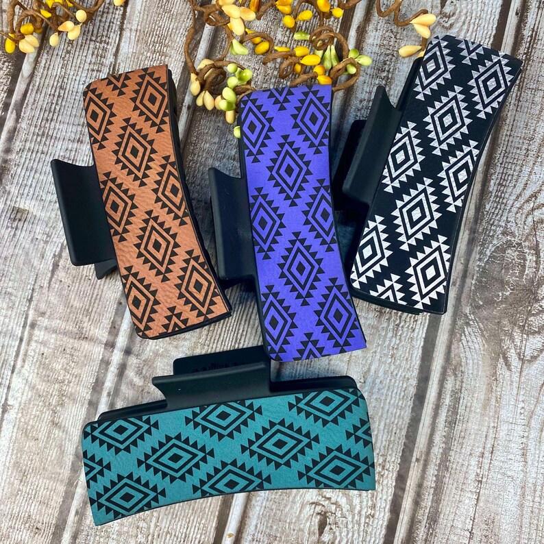 May include: Four hair clips with a geometric pattern. The clips are black with a brown, purple, teal, and black and white geometric pattern.