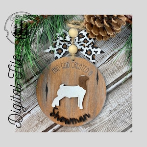 May include: A round wooden ornament featuring a brown and white goat silhouette with the text "And God created a Showman". The ornament is adorned with a brown and white leopard print ribbon and beige beads.