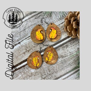 May include: A pair of wooden earrings with a teardrop shape. The earrings are painted with a yellow and orange leaf design and the words "Hello Fall".
