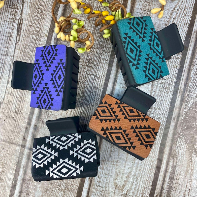 May include: Four hair clips with geometric patterns. The clips are black with a variety of colours and patterns, including purple, teal, brown, and black and white.