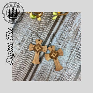 May include: A pair of wooden cross earrings with a geometric pattern. The earrings are brown with a light brown geometric pattern. The earrings are on a wooden background.