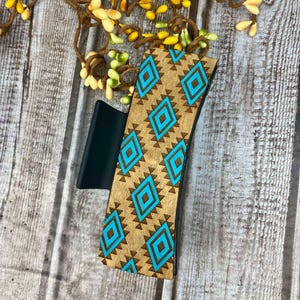 May include: A wooden hair clip with a turquoise and brown geometric pattern. The clip is made of wood and has a black plastic base.