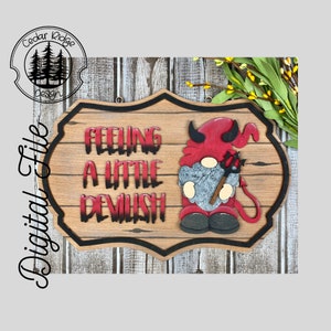 May include: Wooden sign with a rustic woodgrain background. The sign features a red devil gnome with horns and a pitchfork. The text on the sign reads "Feeling a little devilish".