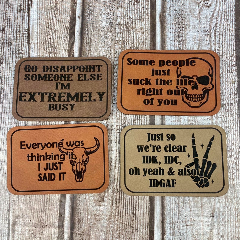May include: Four brown leather patches with black text and images. The patches feature the following sayings: "Go disappoint someone else I'm extremely busy", "Some people just suck the life right out of you", "Everyone was thinking it I just said it", and "Just so we're clear IDK, IDC, oh yeah & also IDGAF".