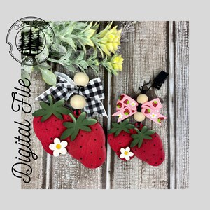 May include: Two wooden strawberry ornaments with black and white checkered and pink bows with white flowers. The ornaments are attached to wooden beads and a black clip.