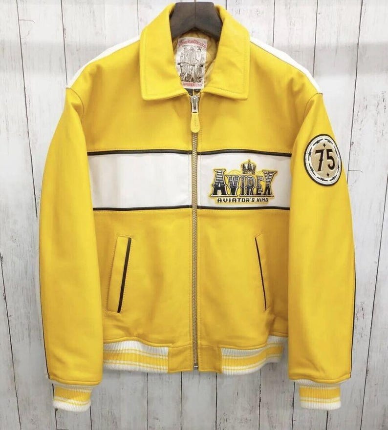 May include: A yellow leather jacket with white stripes and the text "Avirex Aviator's King". The jacket has a collar, zipper, and two front pockets. A patch with the number "75" is on the sleeve.